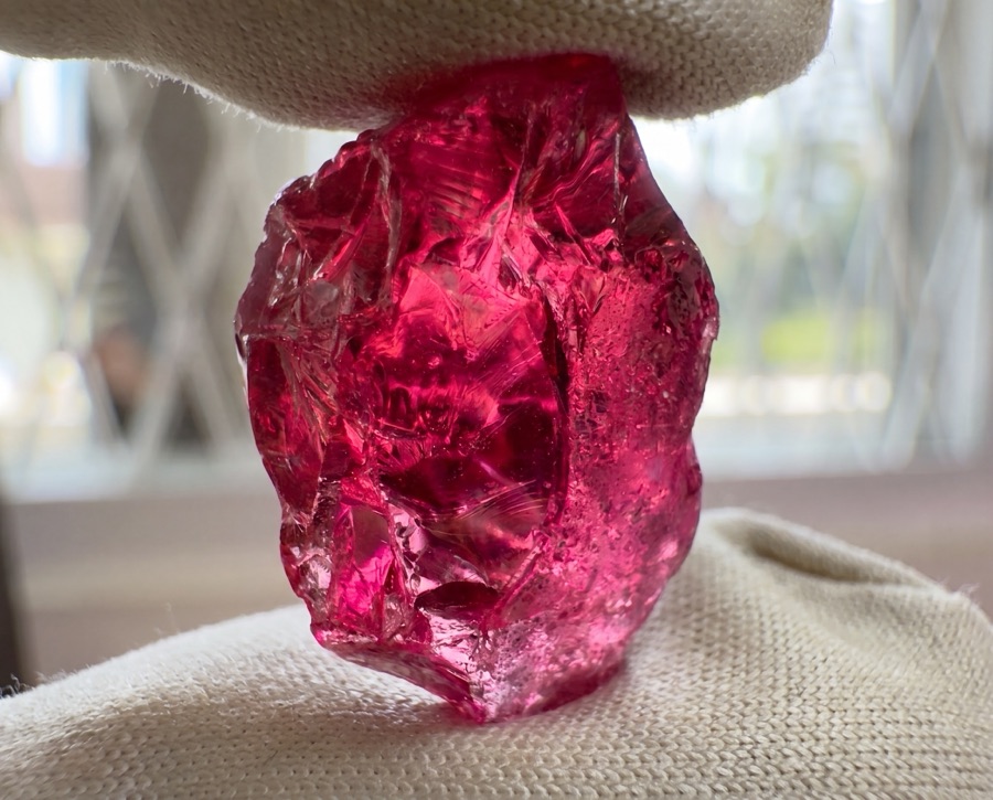 Rough red spinel crystal as found, held in parcel cloth